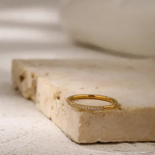 Gold-plated thin ring with small clear stones on textured stone surface