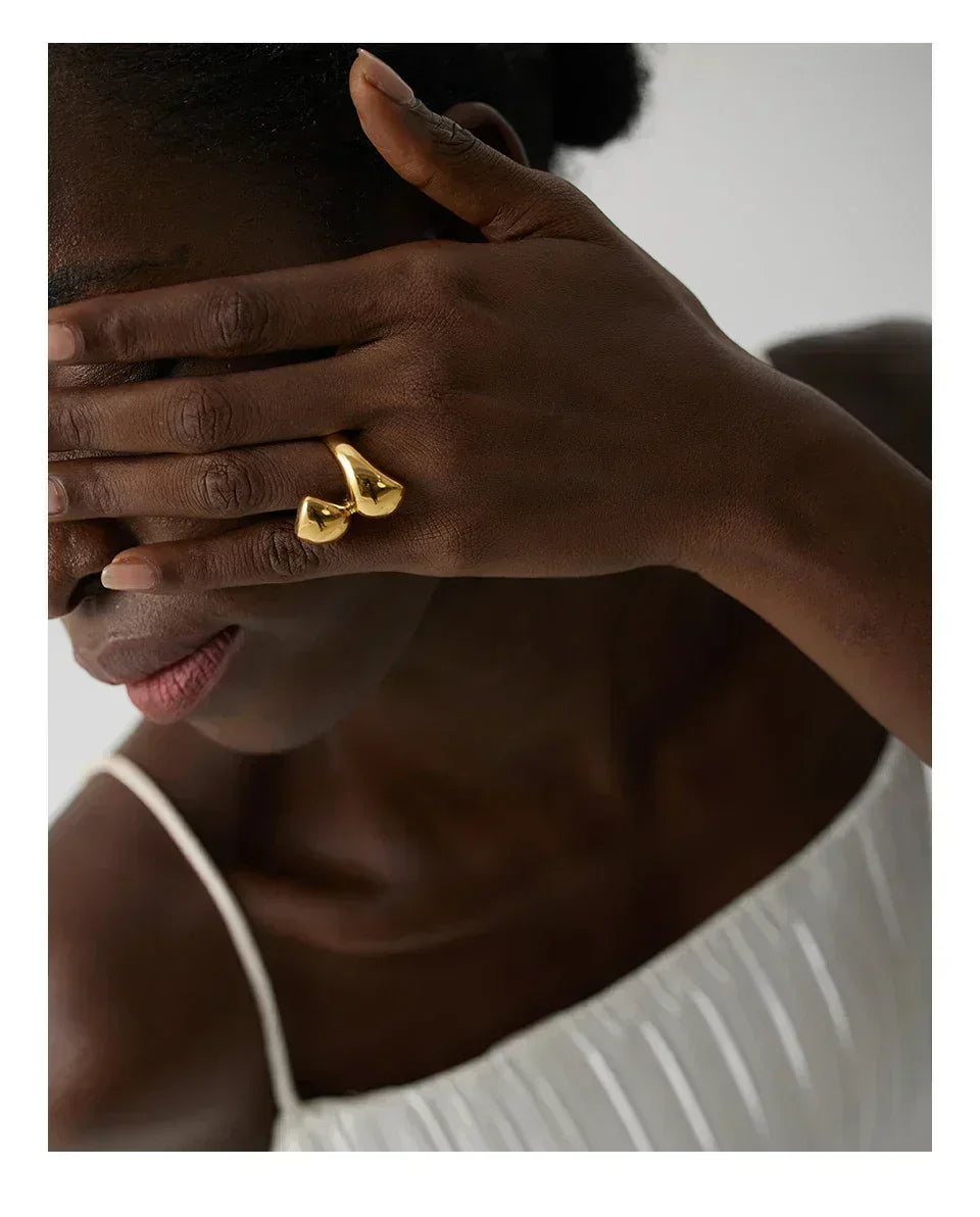 Woman wearing unique gold-plated statement ring on hand, in white pleated dress