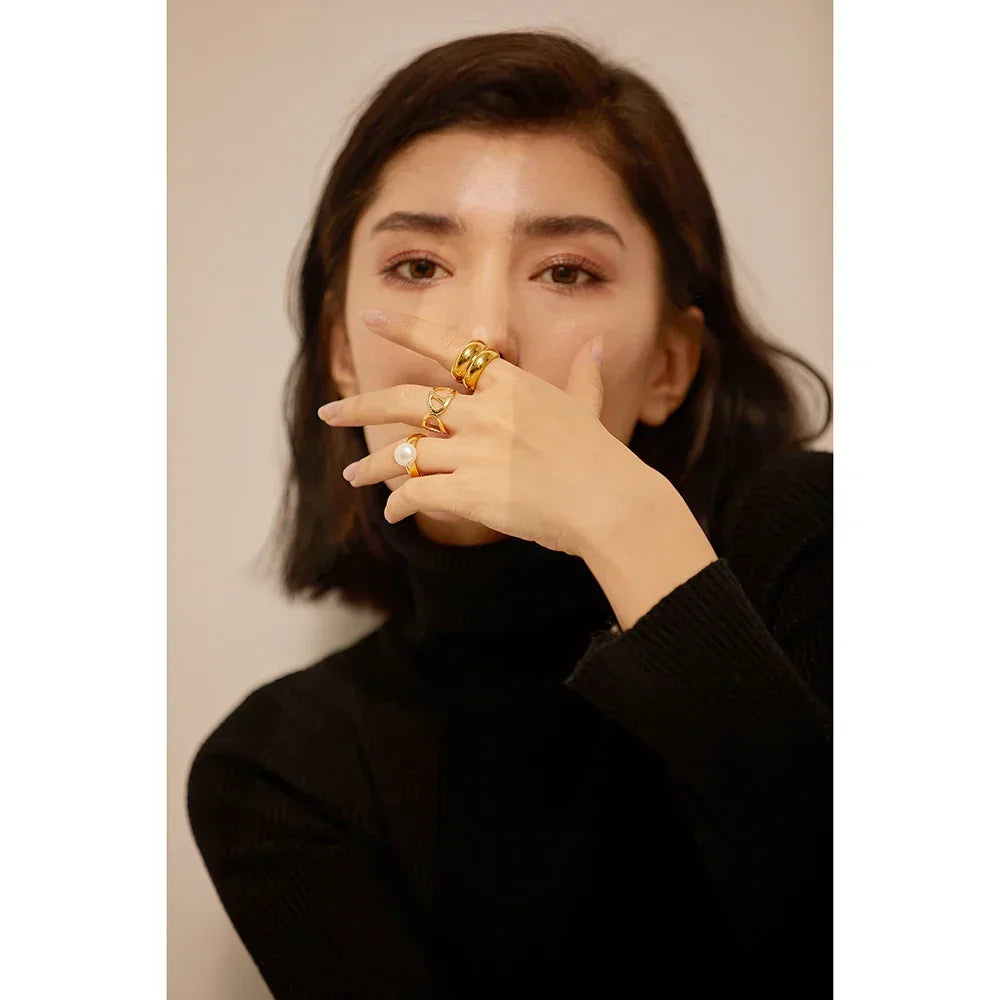 Woman in black sweater wearing multiple gold rings, including pearl and heart designs, on her hand