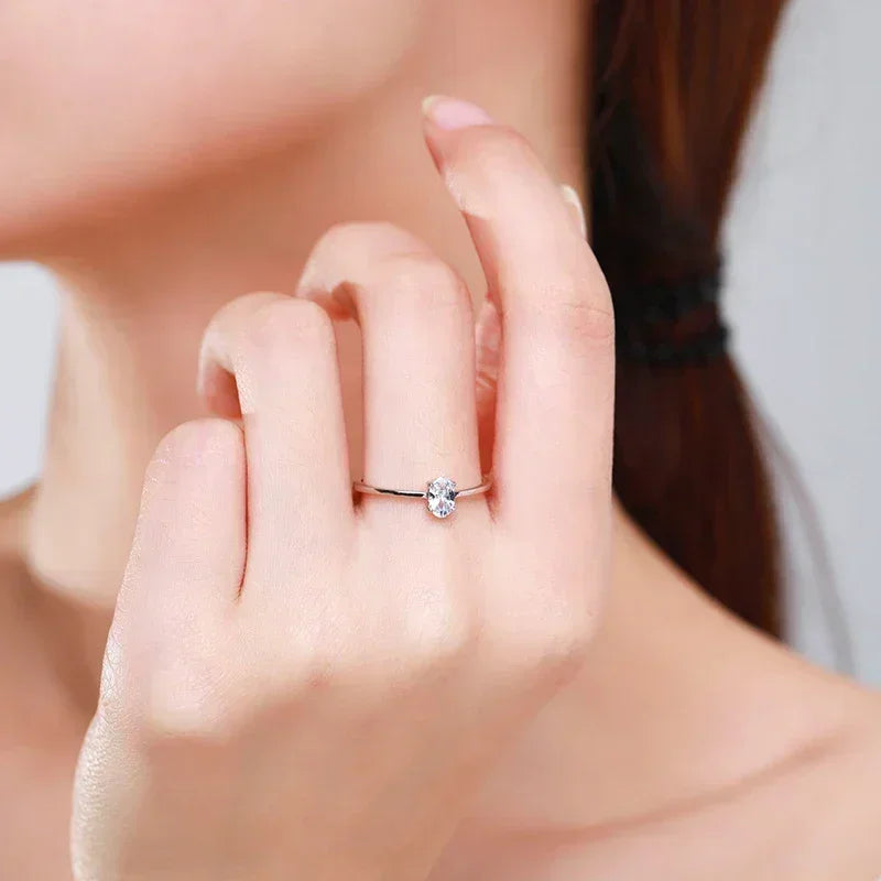 Woman wearing a delicate silver ring with oval clear gemstone on her finger