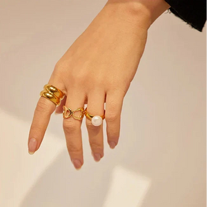 Woman in black sweater wearing multiple gold rings, including pearl and heart designs, on her hand