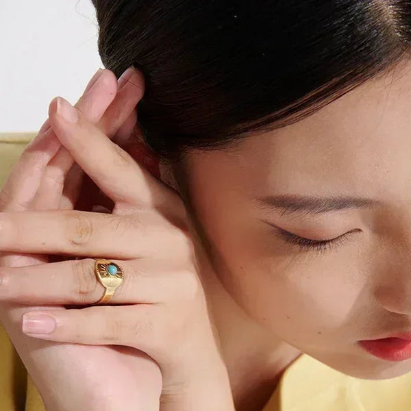 Woman wearing a gold-plated ring with a green gemstone, close-up hand and face