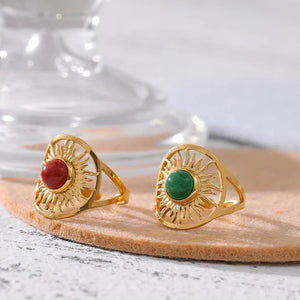 Two gold rings with green and red stones on a wooden surface.