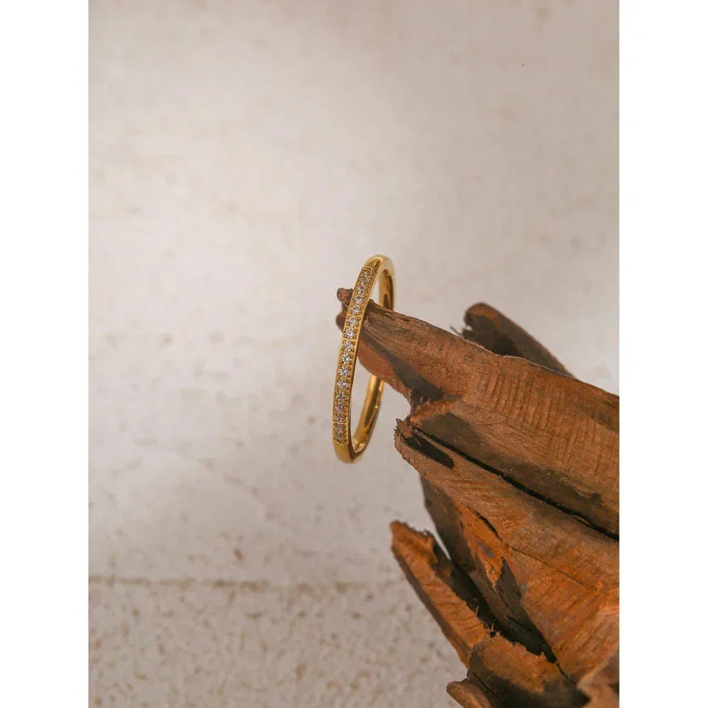 Gold-plated silver ring with small clear stones displayed on wood, elegant jewelry for women