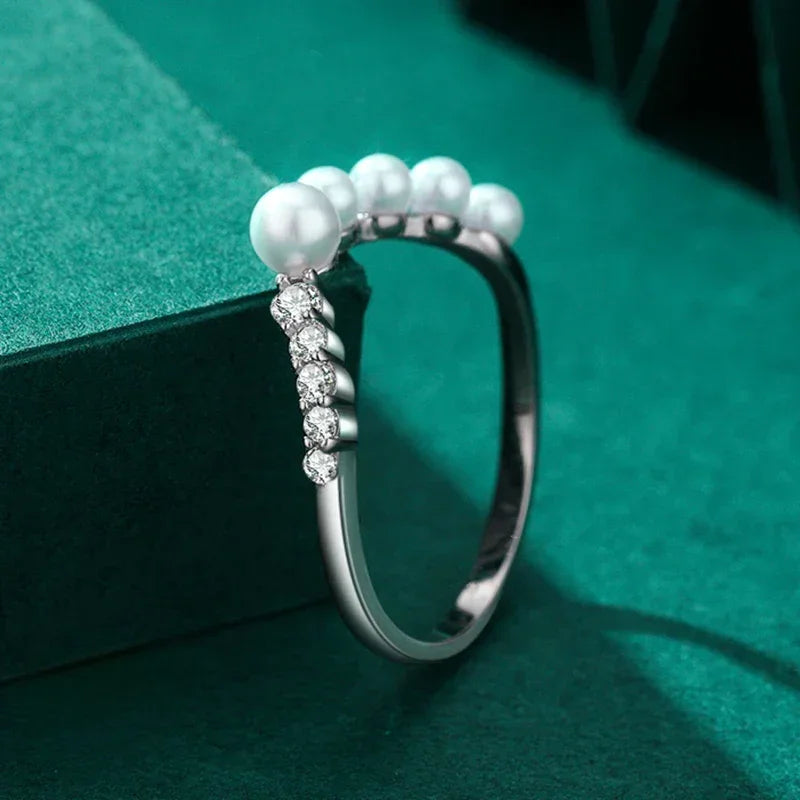 Sterling silver ring with white pearls and sparkling round gemstones on green velvet.