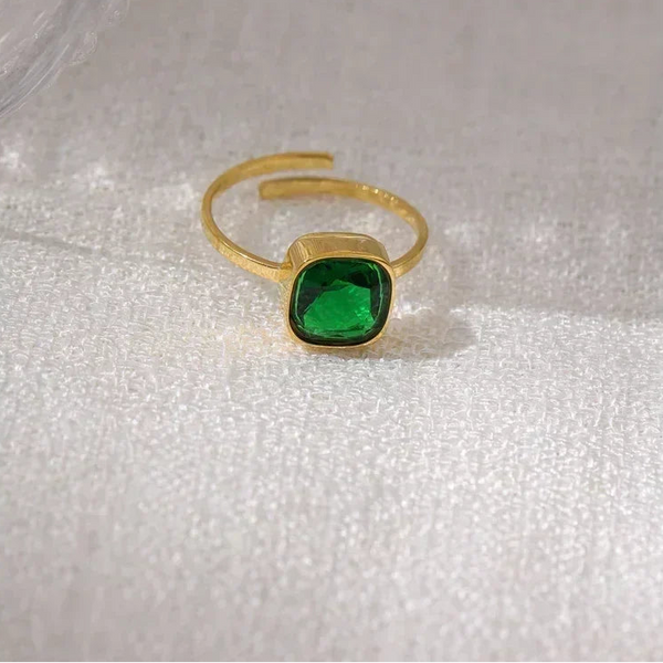 Gold-plated adjustable ring with green square gemstone on white textured fabric