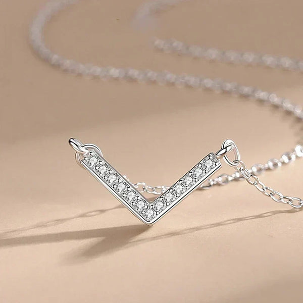 Silver V-shaped necklace with clear stones on a beige background.