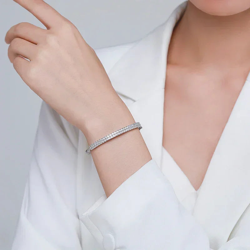 Woman wearing elegant silver tennis bracelet with sparkling crystals, white blouse background