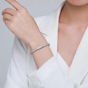 Woman wearing elegant silver tennis bracelet with sparkling crystals, white blouse background
