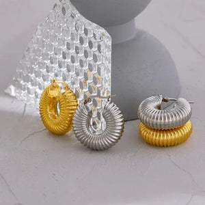 Textured gold and silver hoop earrings displayed on a light gray surface with glass accents.