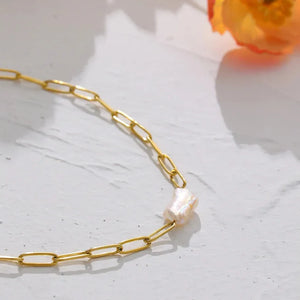 Gold chain necklace with a pearl pendant on a light surface with a flower in the background
