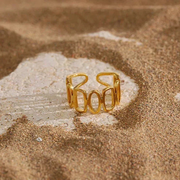 18K gold-plated open ring with geometric design displayed on sandy surface