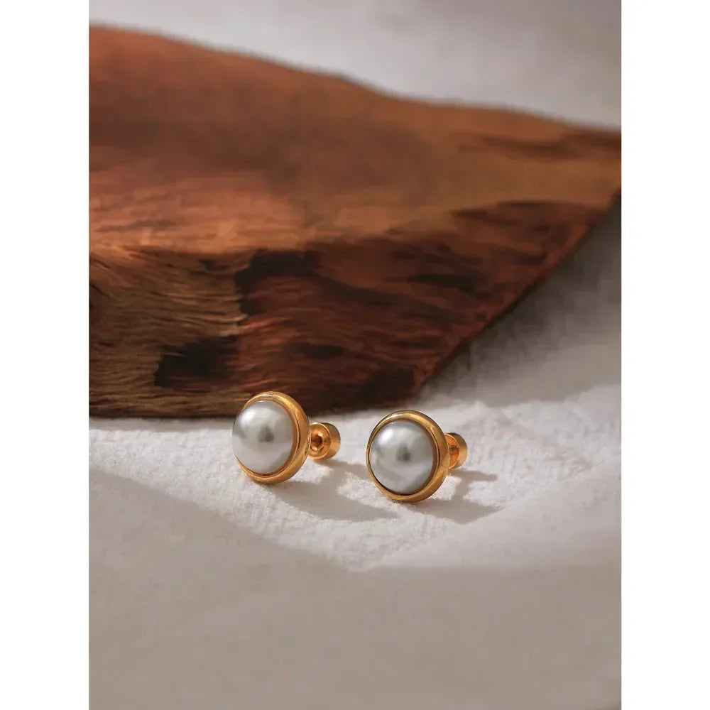 Pair of gold-plated stud earrings with round white pearls on a textured surface