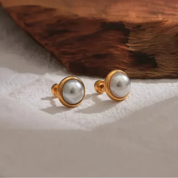 Pair of gold-plated stud earrings with round white pearls on a textured surface