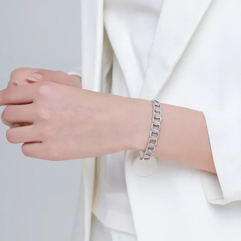 Woman wearing a silver chain link bracelet with sparkling accents, styled with a white blazer.
