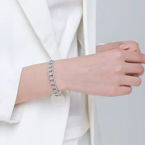 Woman wearing a silver chain link bracelet with sparkling accents, styled with a white blazer.