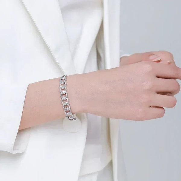 Woman wearing a silver chain link bracelet with sparkling accents, styled with a white blazer.