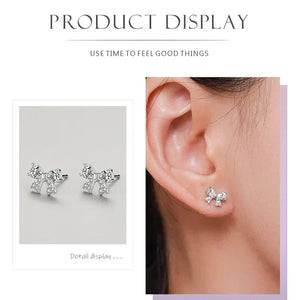Silver bow-shaped earrings displayed on a gray background and worn on an ear.
