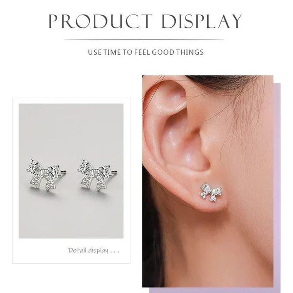 Silver bow-shaped earrings displayed on a gray background and worn on an ear.