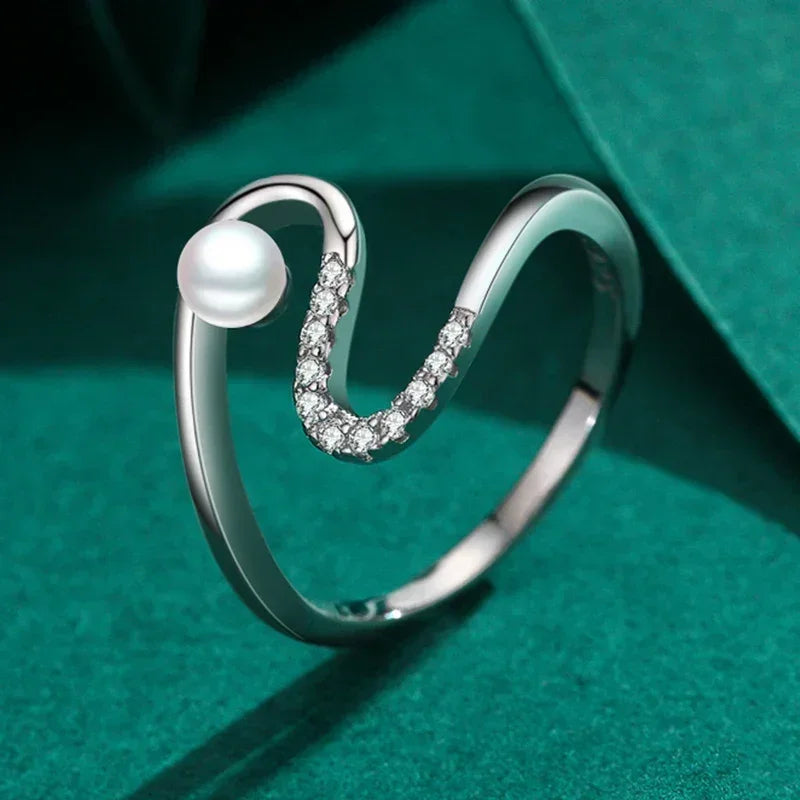Sterling silver wave ring with pearl and cubic zirconia accents on green background