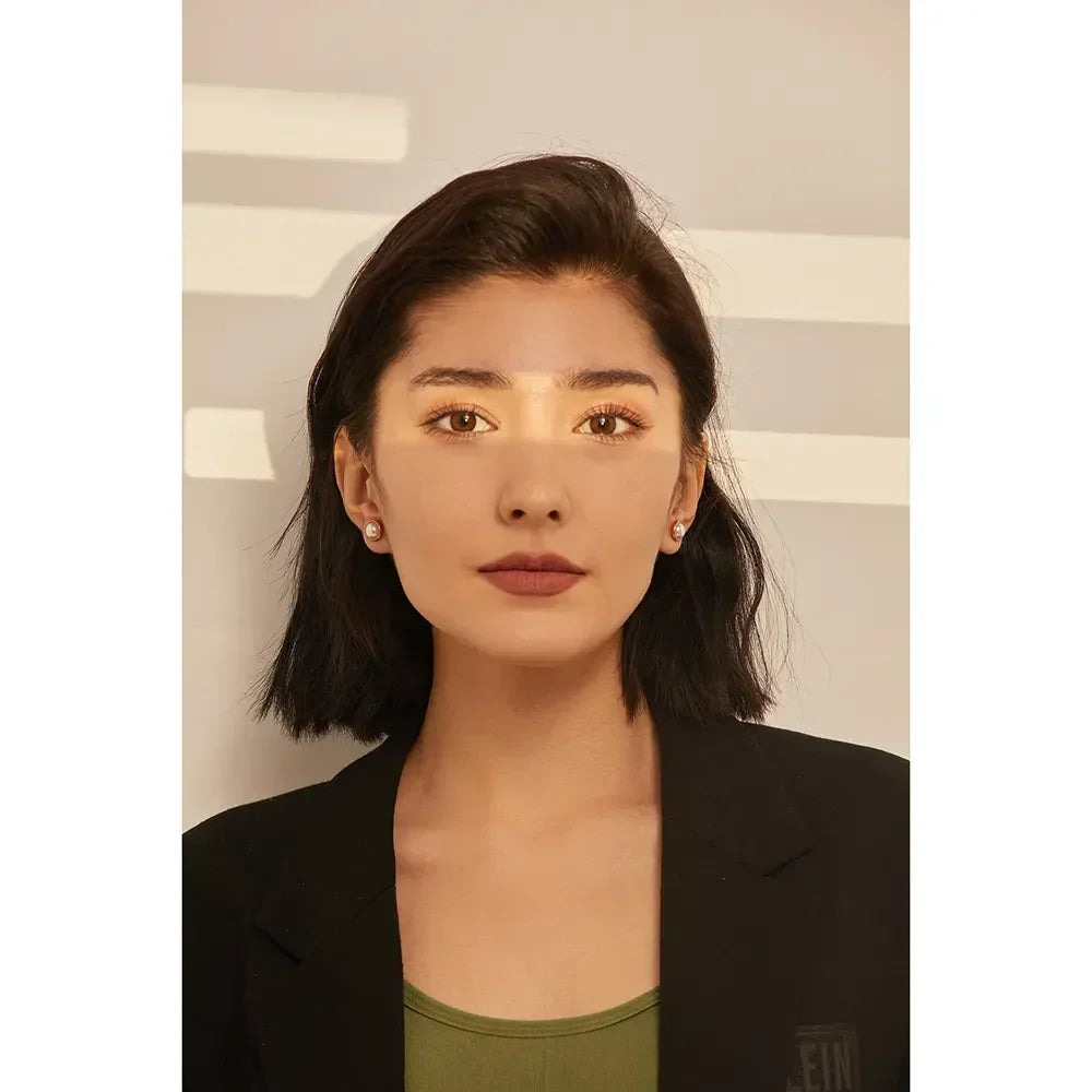 Woman wearing pearl stud earrings, black blazer, and green top, with sunlight on her face