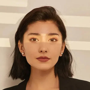 Woman wearing pearl stud earrings, black blazer, and green top, with sunlight on her face