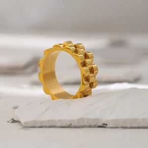 Gold-plated geometric band ring with scalloped edges on a neutral background