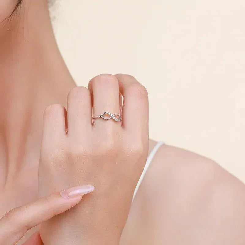 Woman wearing a delicate infinity symbol silver ring on her finger against a neutral background