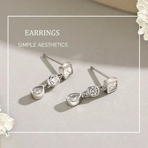 Silver earrings with teardrop and square designs on a light gray background with floral elements.