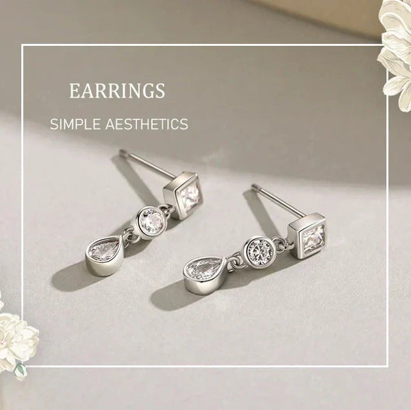Silver earrings with teardrop and square designs on a light gray background with floral elements.