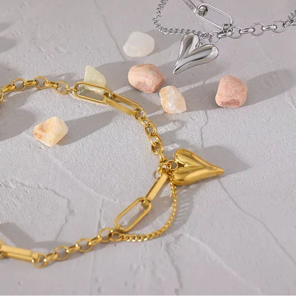 Gold and silver heart bracelets with chunky chain links on stone background with scattered pebbles