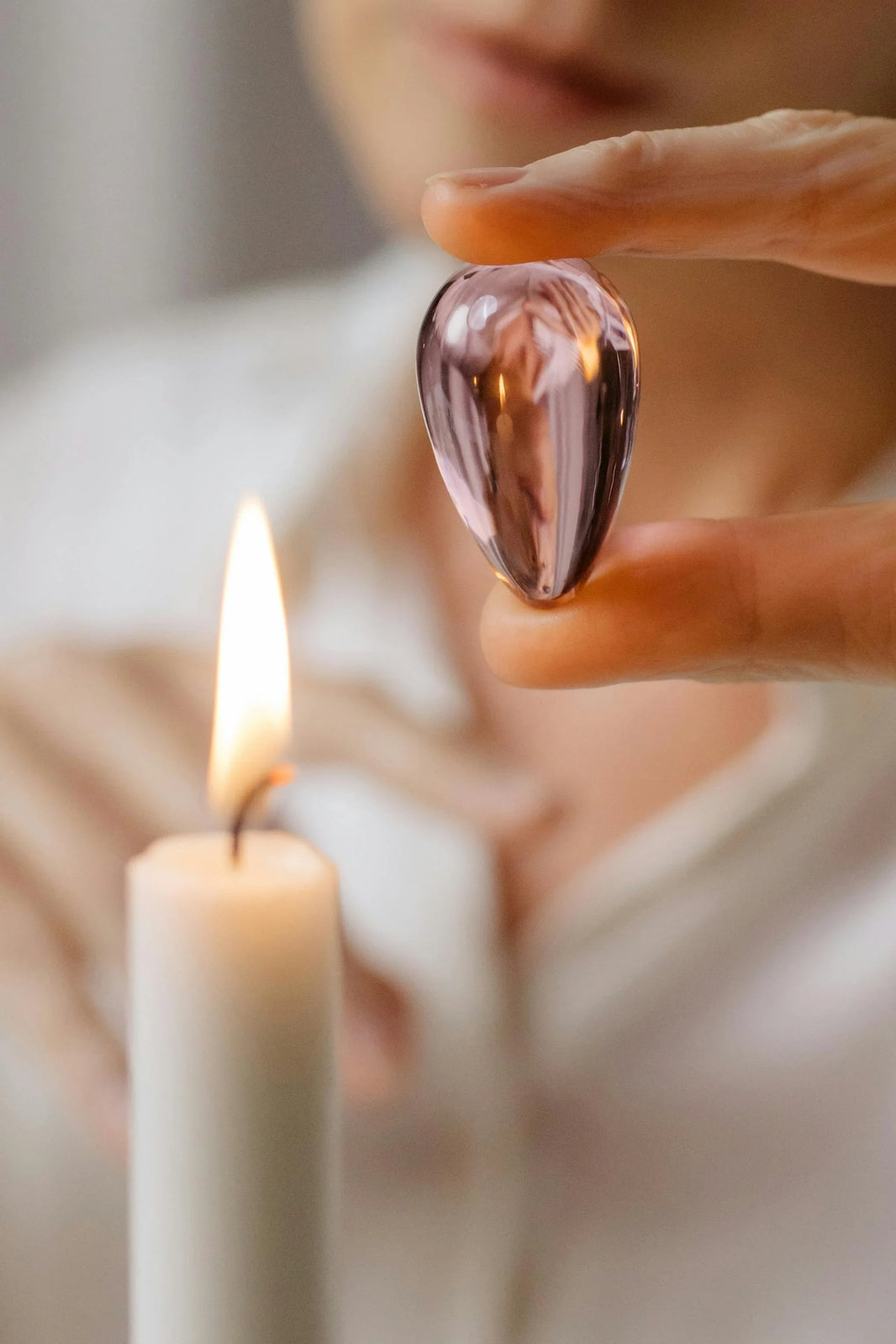 Hand holding a pink crystal ball near a lit candle