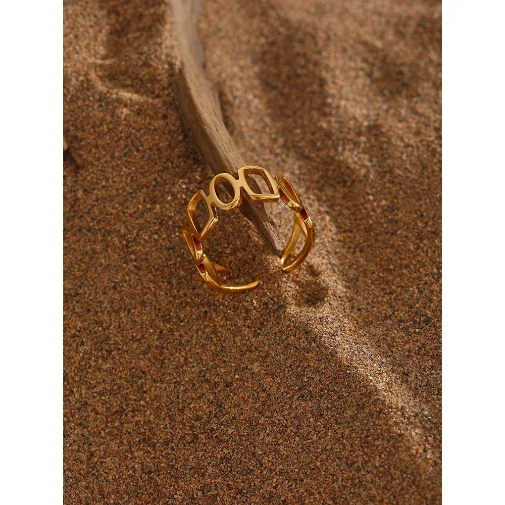 Open gold-plated geometric ring on sand with driftwood accent, elegant women's jewelry