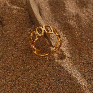 Open gold-plated geometric ring on sand with driftwood accent, elegant women's jewelry