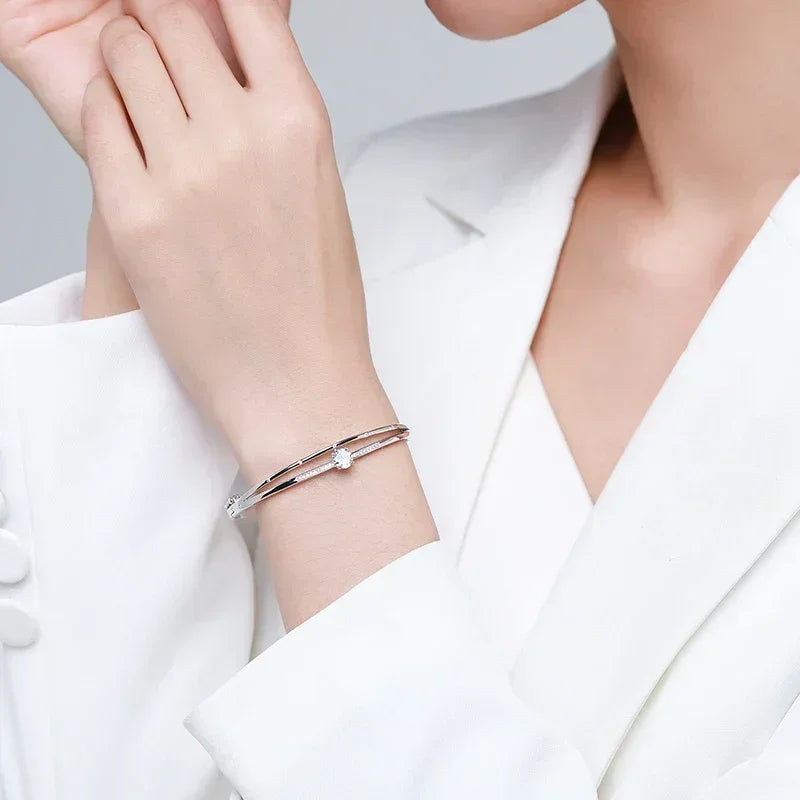 Elegant woman wearing a minimalist silver bracelet with a central gemstone, white suit.