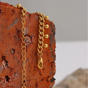 Gold chain necklace on a textured orange surface with 'DESIGN DETAILS' text.