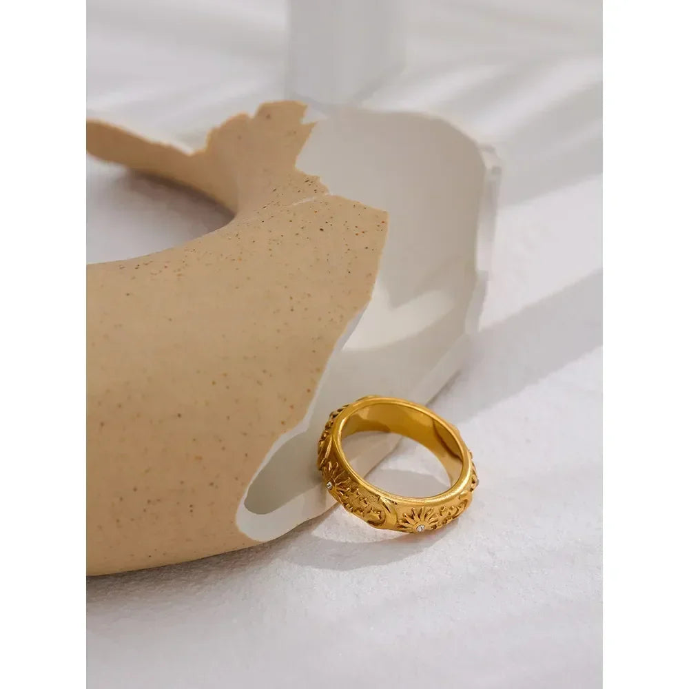 Gold-plated floral engraved ring on a textured ceramic surface, elegant jewelry design