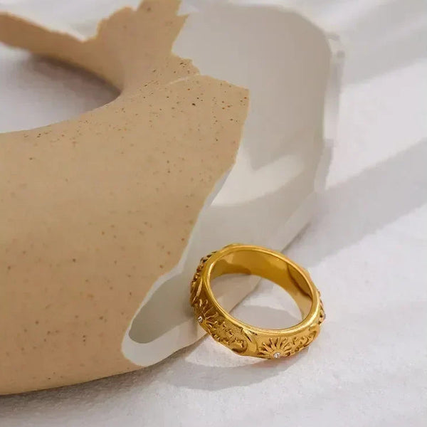 Gold-plated floral engraved ring on a textured ceramic surface, elegant jewelry design