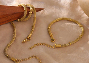 Gold bracelets on a textured beige surface with a wooden stick.