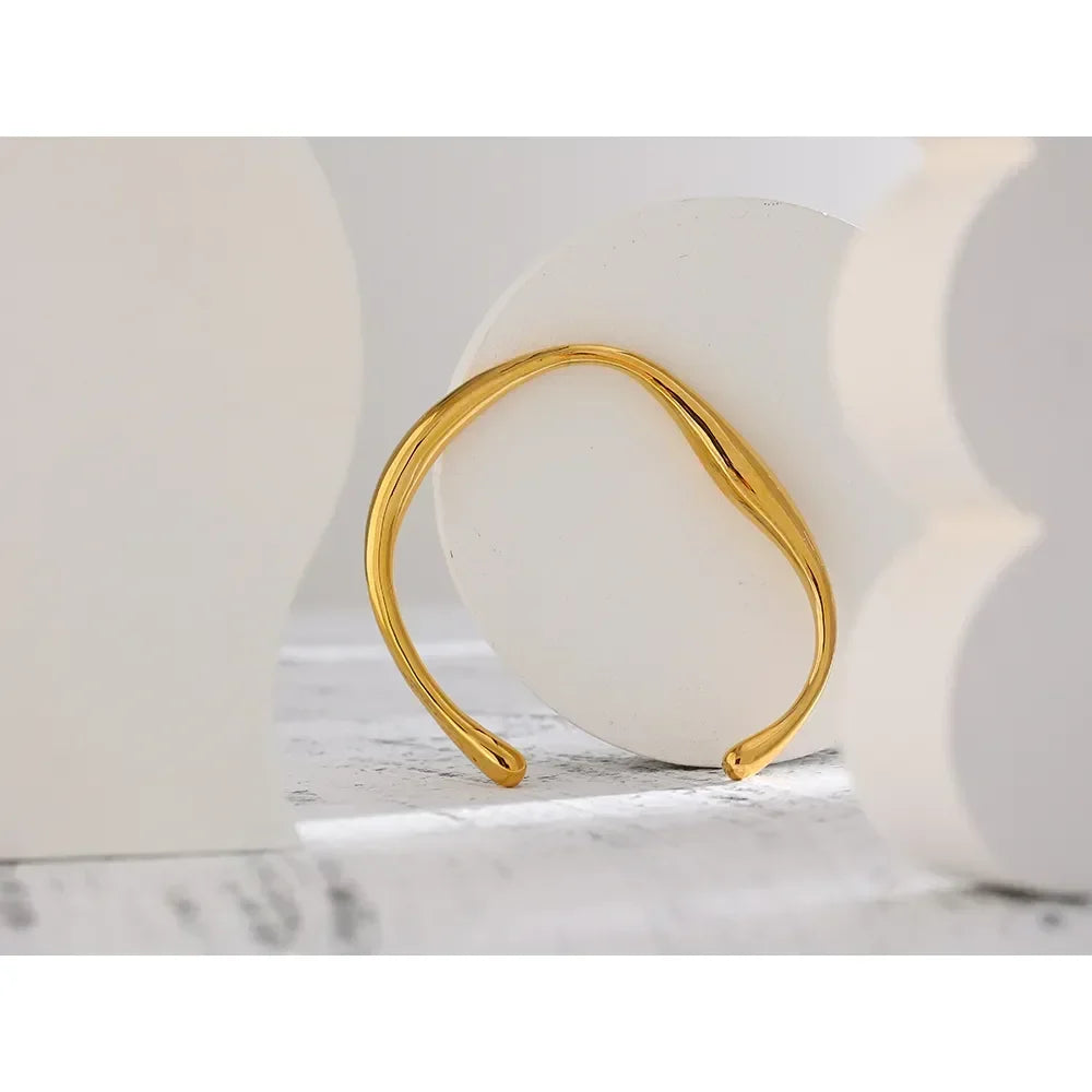 Elegant 18K gold-plated open cuff bracelet with a wavy design on a neutral background
