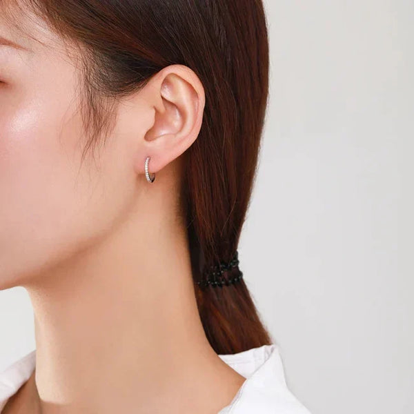 Close-up of a person wearing a silver hoop earring on a plain background
