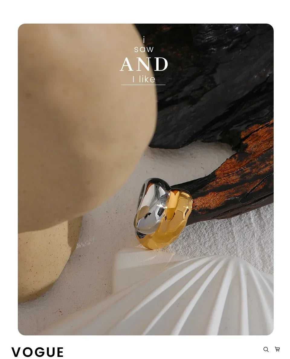 Chunky two-tone gold and silver ring on textured white surface with organic elements