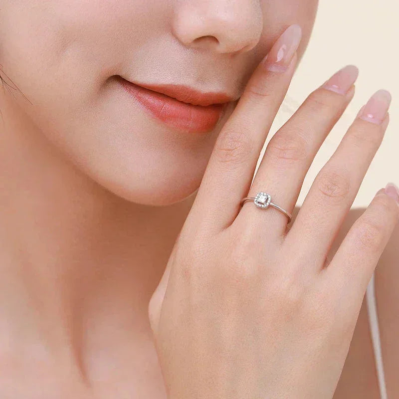 Woman wearing a delicate silver engagement ring with a square-cut gemstone