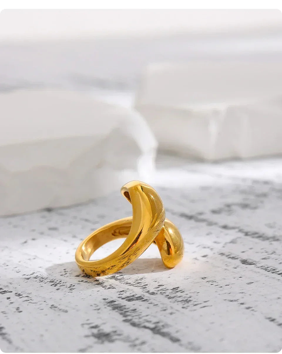 Elegant 18K gold-plated open ring with a modern sculptural twist design on a textured surface
