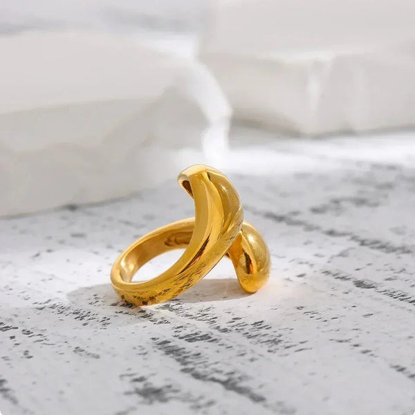 Elegant 18K gold-plated open ring with a modern sculptural twist design on a textured surface