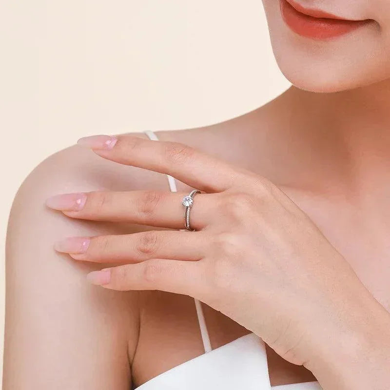 Woman wearing a silver engagement ring with a round solitaire stone on her finger.