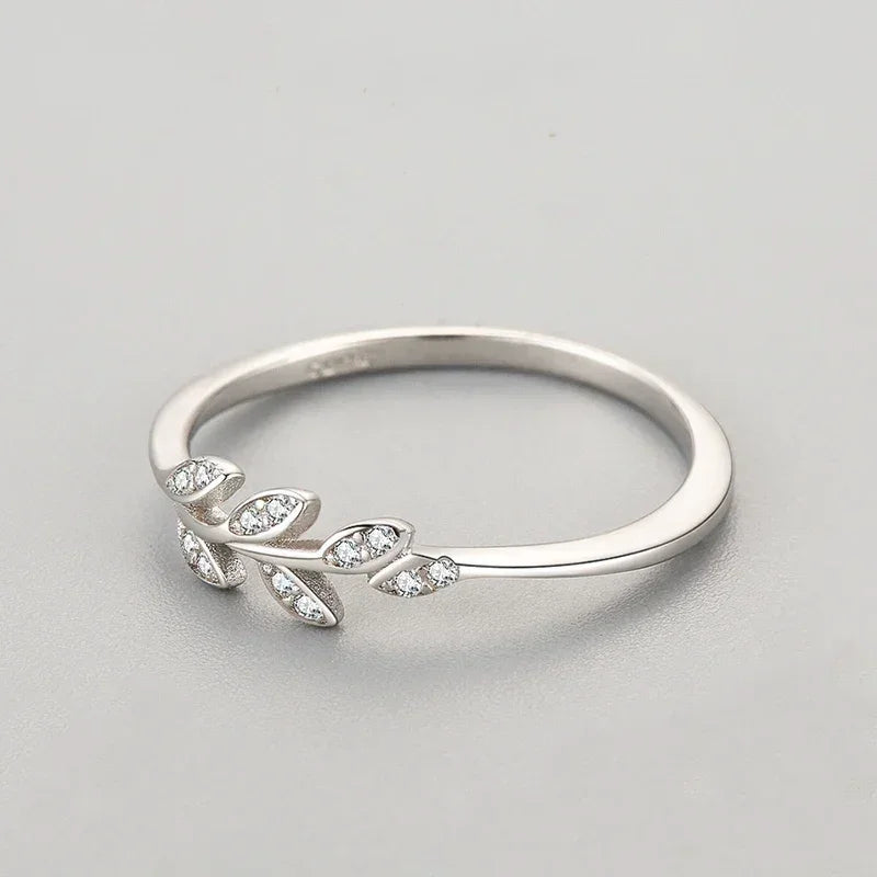 Sterling silver ring with leaf design and small clear gemstones on light background