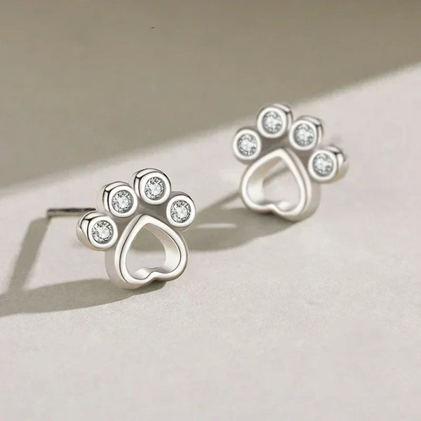 Silver paw-shaped earrings with clear gemstones on a light background