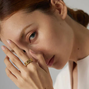 Woman wearing a chunky gold-plated chain ring, touching her lips, elegant neutral background