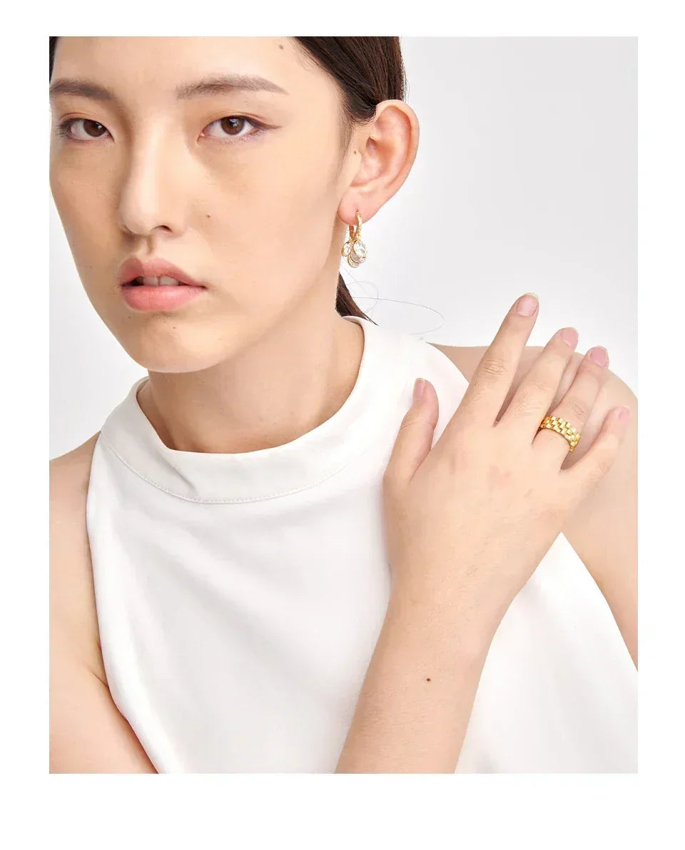 Woman wearing gold-plated hoop earrings and textured gold ring, white sleeveless top
